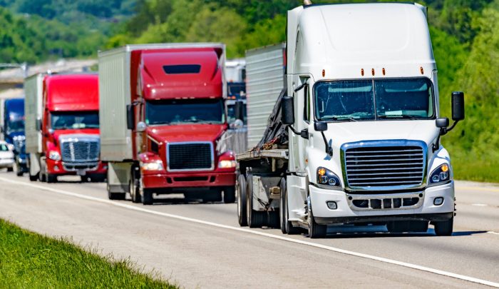 A solid line of eighteen-wheelers barrel down an interstate highway in Tennessee.  Heat waves rising from the pavement give a nice shimmering effect to vehicles and trees behind the lead truck.