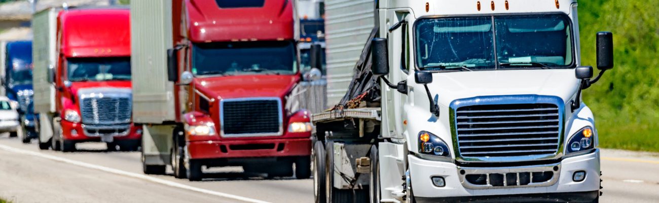 A solid line of eighteen-wheelers barrel down an interstate highway in Tennessee.  Heat waves rising from the pavement give a nice shimmering effect to vehicles and trees behind the lead truck.